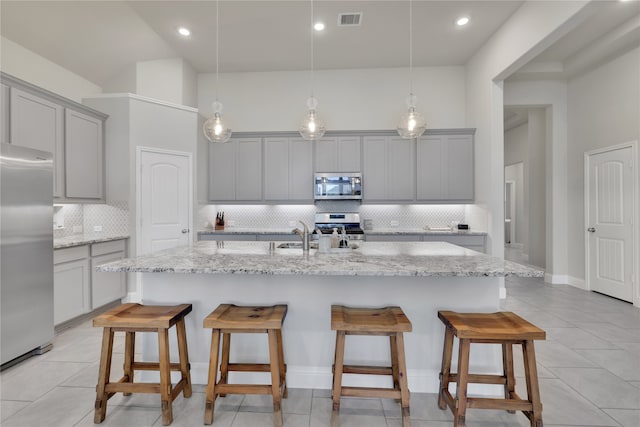 kitchen with gray cabinets, stainless steel appliances, and a center island with sink