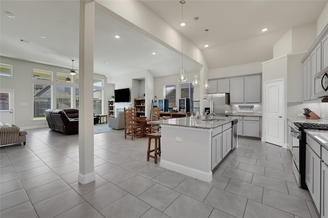 kitchen with a center island with sink, light stone counters, gray cabinets, ceiling fan, and appliances with stainless steel finishes