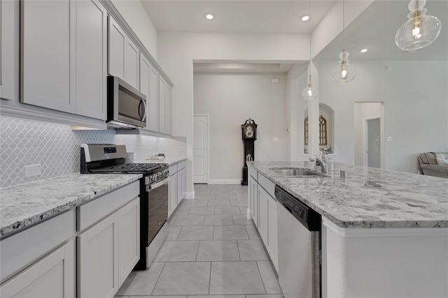 kitchen featuring decorative backsplash, light tile patterned floors, an island with sink, pendant lighting, and appliances with stainless steel finishes