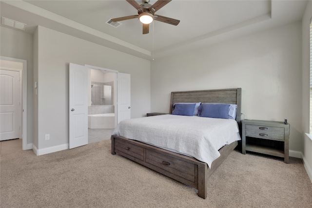 bedroom with a raised ceiling, light carpet, ceiling fan, and ensuite bath