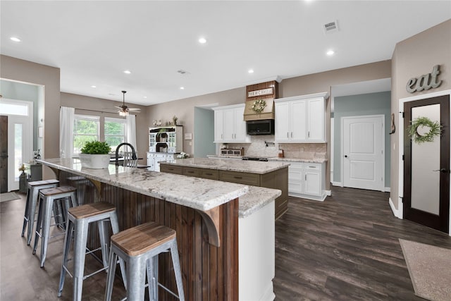 kitchen with light stone counters, dark hardwood / wood-style flooring, white cabinets, a breakfast bar area, and a spacious island