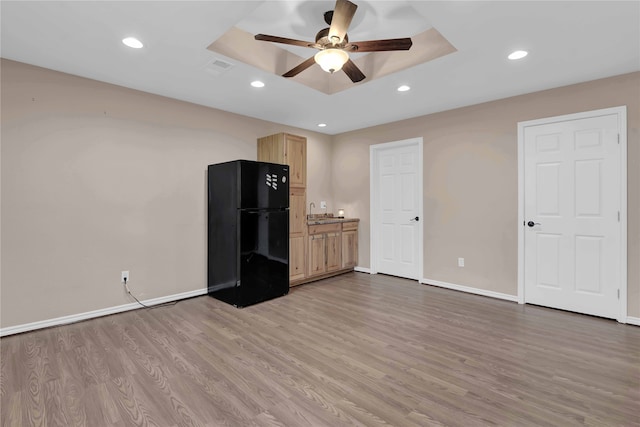 interior space with a tray ceiling, black fridge, light brown cabinets, and light wood-type flooring