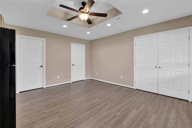 unfurnished bedroom with ceiling fan, black fridge, light wood-type flooring, and a tray ceiling