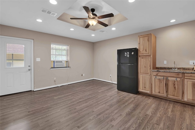 kitchen with dark stone countertops, ceiling fan, a tray ceiling, dark wood-type flooring, and black refrigerator