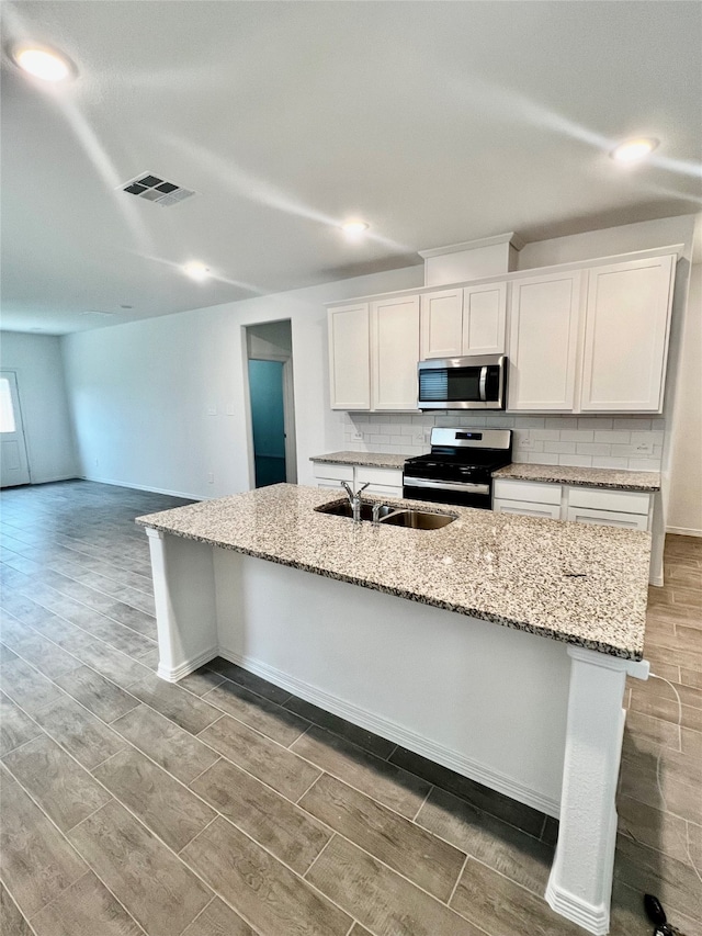 kitchen featuring white cabinets, hardwood / wood-style flooring, an island with sink, and appliances with stainless steel finishes