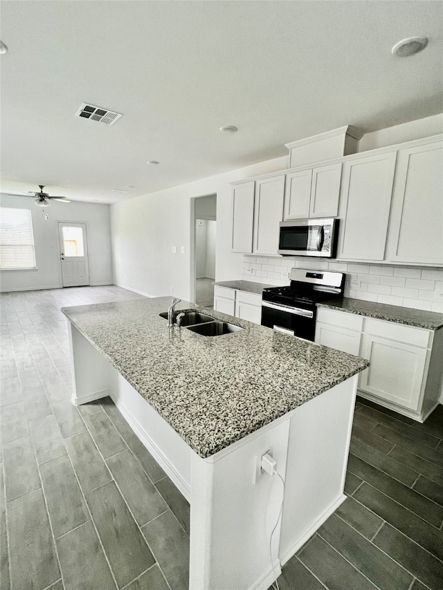 kitchen with white cabinetry, sink, stove, and a kitchen island with sink