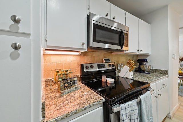 kitchen featuring tasteful backsplash, light stone countertops, white cabinetry, light wood-type flooring, and appliances with stainless steel finishes