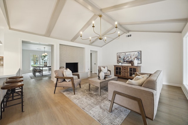 living room featuring lofted ceiling with beams, a chandelier, hardwood / wood-style flooring, and a brick fireplace