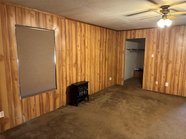 interior space with carpet flooring, wood walls, a textured ceiling, and a wood stove