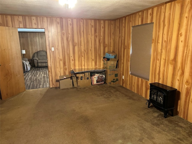 interior space featuring wood walls, carpet floors, a textured ceiling, and a wood stove