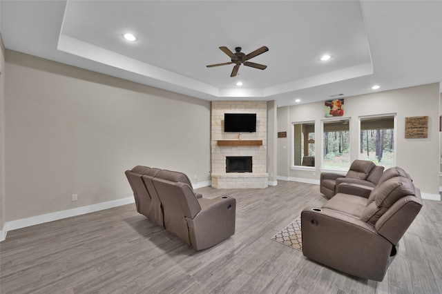 living room with ceiling fan, light hardwood / wood-style floors, a stone fireplace, and a raised ceiling