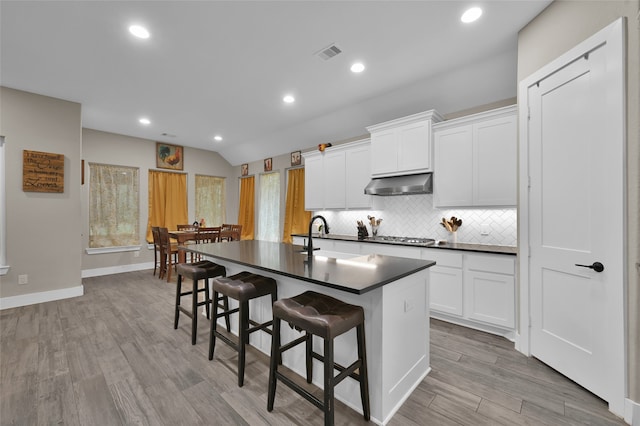 kitchen with light hardwood / wood-style floors, white cabinetry, extractor fan, a kitchen breakfast bar, and an island with sink