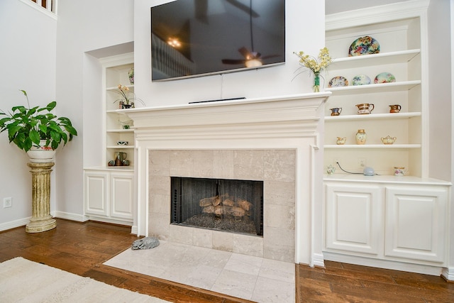 room details featuring a tiled fireplace, wood finished floors, built in features, and baseboards