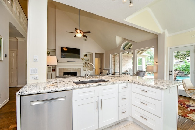 kitchen featuring a tile fireplace, a sink, open floor plan, light stone countertops, and dishwasher