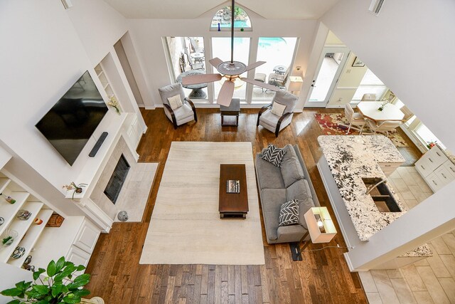 living room with a high ceiling, ceiling fan, a tiled fireplace, and dark hardwood / wood-style flooring