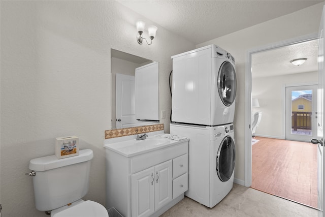 washroom with a textured ceiling, sink, stacked washer and dryer, and light hardwood / wood-style flooring