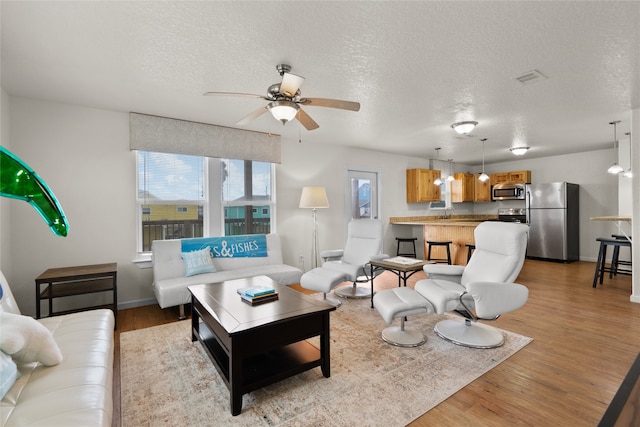 living room featuring a textured ceiling, light hardwood / wood-style floors, and ceiling fan