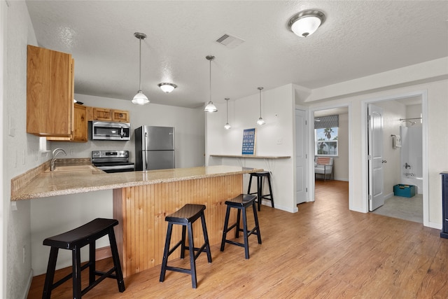 kitchen with kitchen peninsula, appliances with stainless steel finishes, a kitchen bar, light wood-type flooring, and sink