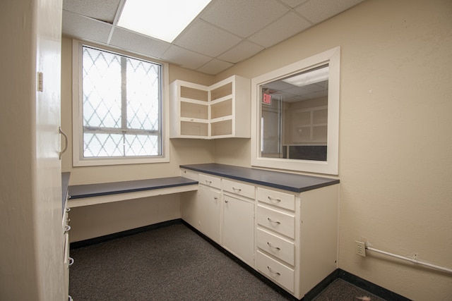 kitchen with white cabinetry, dark carpet, and a drop ceiling