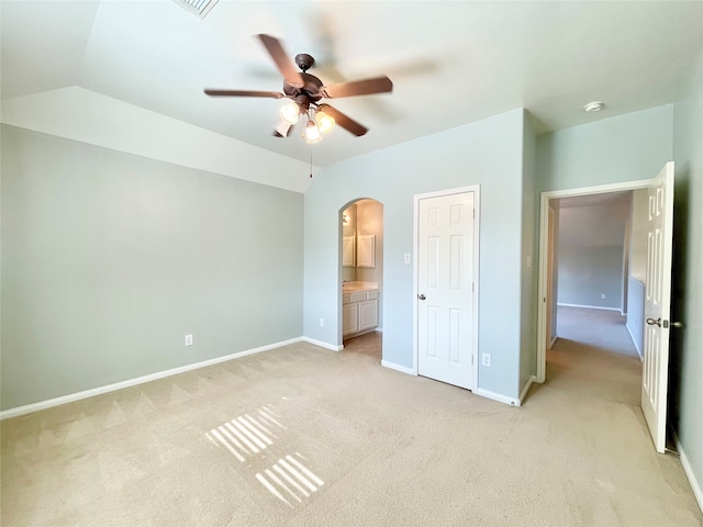 unfurnished bedroom featuring ensuite bathroom, ceiling fan, light colored carpet, and lofted ceiling