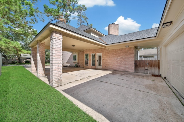 back of property featuring driveway, brick siding, a chimney, and a lawn