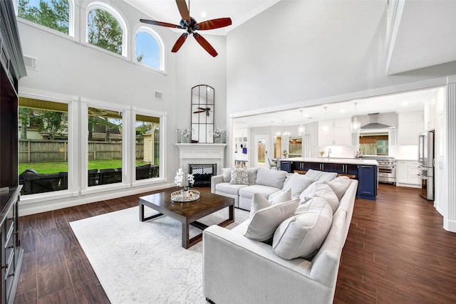 living room featuring ceiling fan, a healthy amount of sunlight, dark hardwood / wood-style flooring, and a towering ceiling