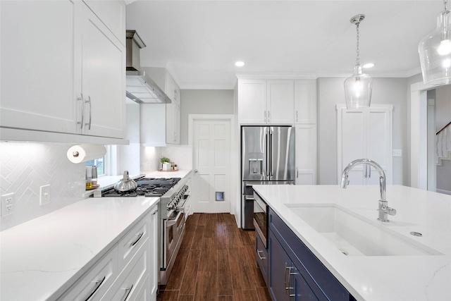 kitchen featuring premium appliances, blue cabinetry, white cabinetry, a sink, and wall chimney exhaust hood