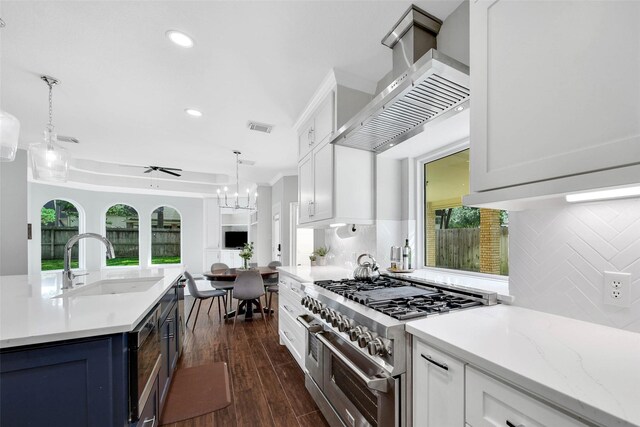 kitchen with white cabinets, range with two ovens, sink, wall chimney exhaust hood, and ceiling fan