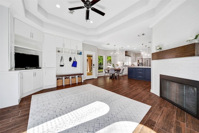 living room featuring a fireplace, a raised ceiling, ceiling fan, and ornamental molding