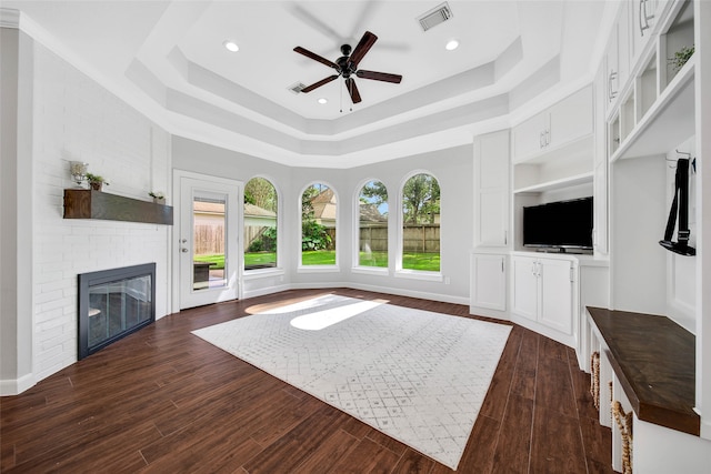 unfurnished living room featuring a brick fireplace, dark hardwood / wood-style floors, a raised ceiling, and ceiling fan