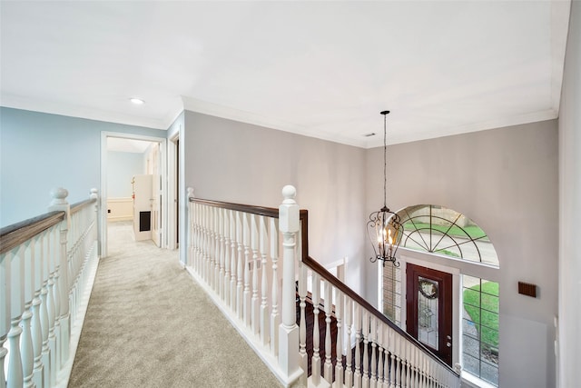 corridor with a notable chandelier, light colored carpet, and crown molding