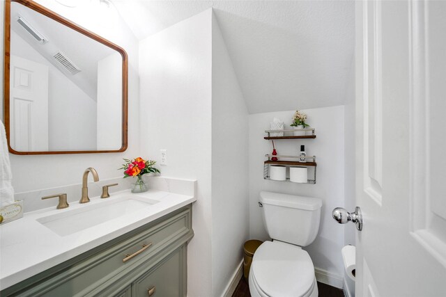 half bath featuring lofted ceiling, visible vents, toilet, and vanity