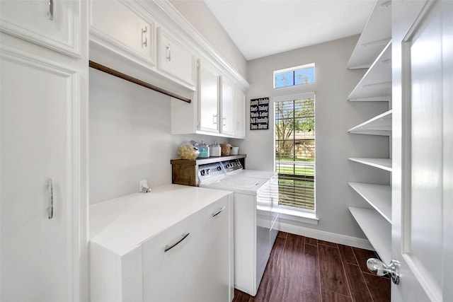 clothes washing area featuring dark wood-type flooring, washing machine and clothes dryer, cabinet space, and baseboards