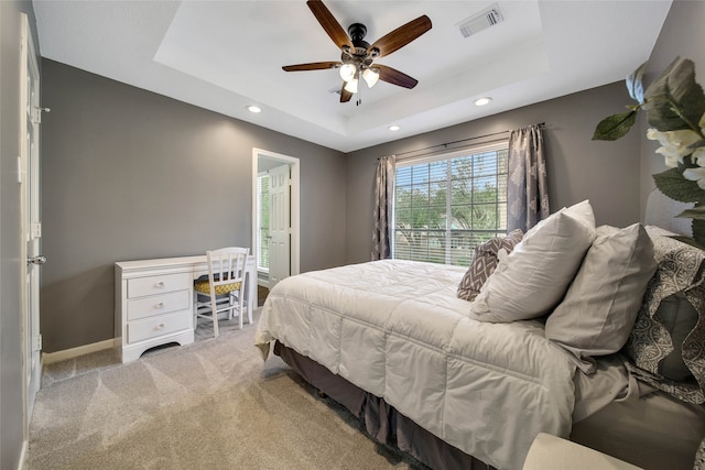 bedroom featuring light colored carpet, a raised ceiling, and ceiling fan