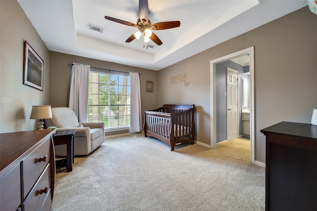 bedroom with light carpet, ensuite bathroom, a raised ceiling, ceiling fan, and a nursery area