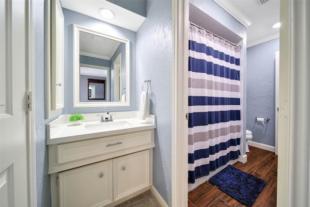 bathroom featuring a textured wall, toilet, ornamental molding, vanity, and wood finished floors