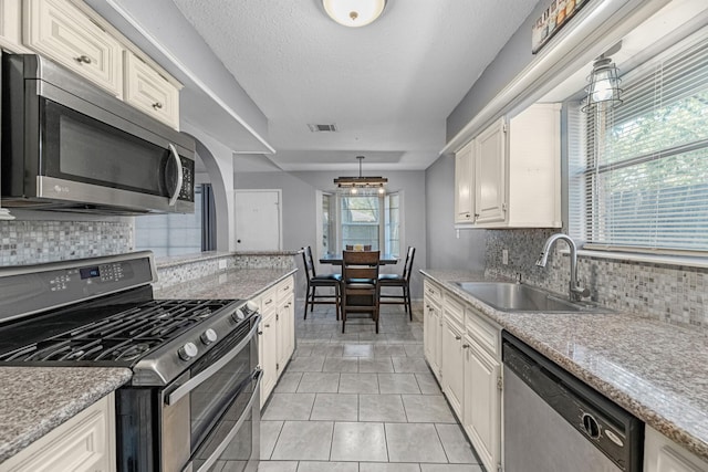kitchen with appliances with stainless steel finishes, a sink, decorative backsplash, light tile patterned flooring, and a textured ceiling