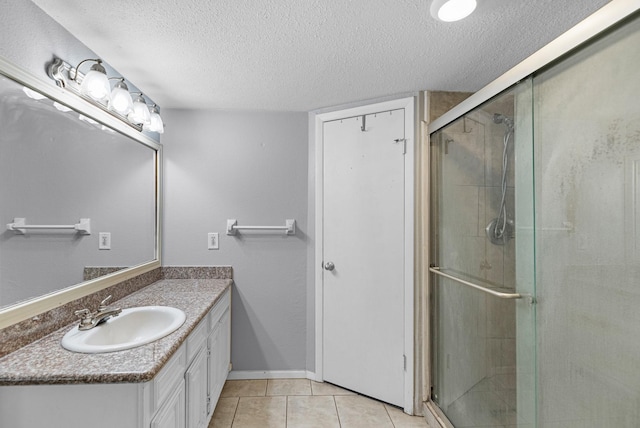bathroom with a textured ceiling, a stall shower, vanity, tile patterned flooring, and baseboards