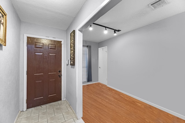 foyer entrance featuring rail lighting, light wood-type flooring, and a textured ceiling