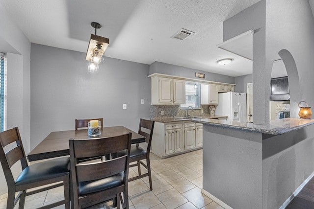 kitchen featuring white fridge with ice dispenser, a sink, cream cabinetry, decorative backsplash, and a textured ceiling