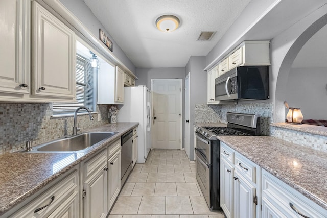 kitchen with stainless steel appliances, a sink, backsplash, arched walkways, and light tile patterned flooring