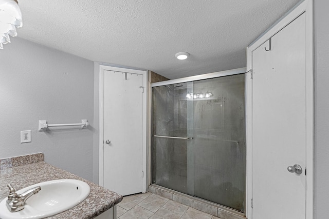 full bathroom featuring a textured ceiling, a stall shower, vanity, and tile patterned floors