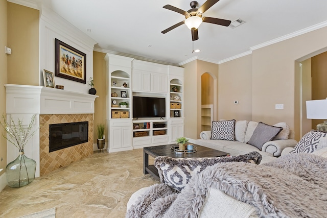 living room with built in features, a tiled fireplace, ceiling fan, and crown molding