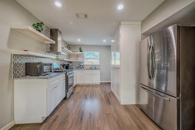 kitchen featuring white cabinets, wall chimney exhaust hood, light wood-type flooring, appliances with stainless steel finishes, and tasteful backsplash