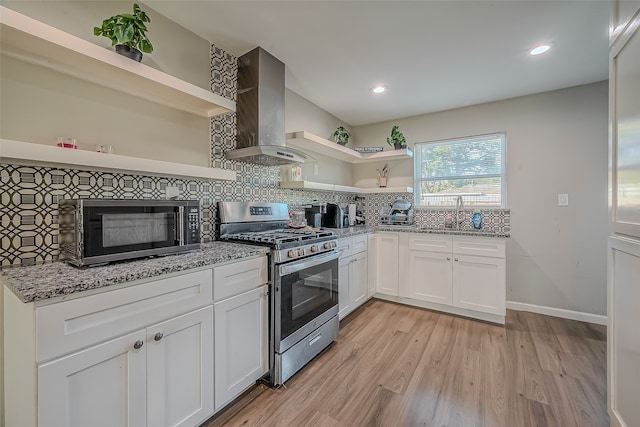 kitchen featuring white cabinetry, sink, wall chimney range hood, light stone counters, and appliances with stainless steel finishes