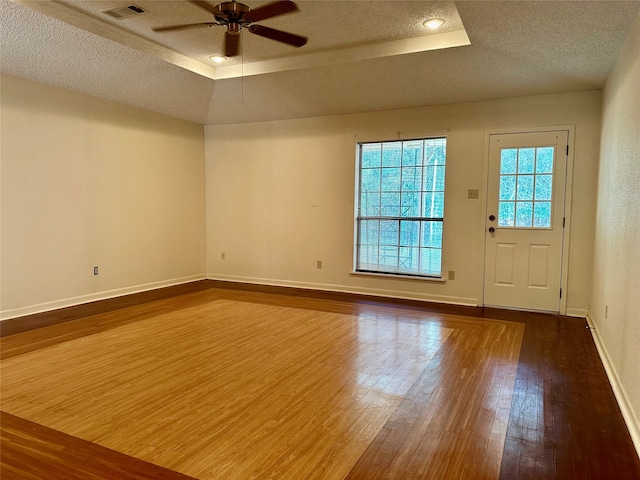 unfurnished room featuring a textured ceiling, wood-type flooring, ceiling fan, and a raised ceiling