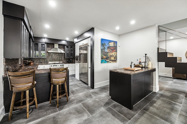 kitchen with a kitchen bar, high end appliances, kitchen peninsula, tasteful backsplash, and wall chimney range hood