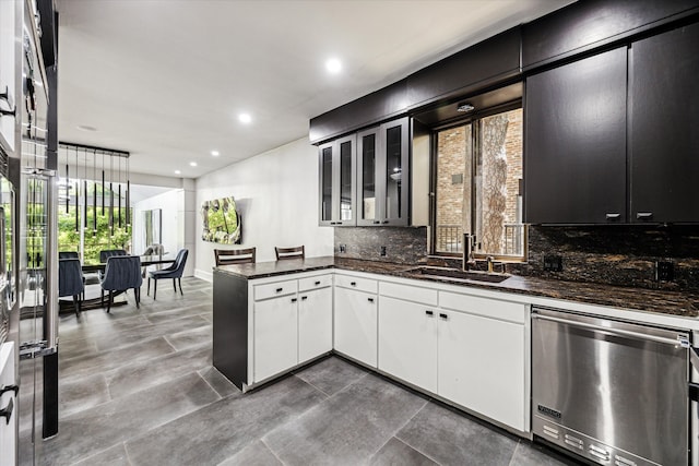 kitchen featuring dark stone counters, backsplash, sink, white cabinets, and kitchen peninsula