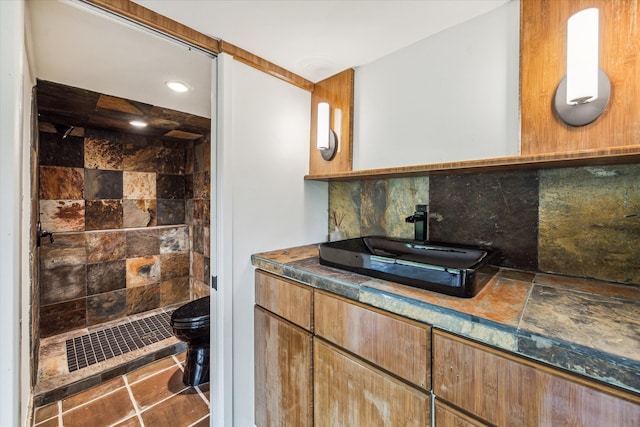 bathroom with toilet, decorative backsplash, tile patterned flooring, vanity, and a shower