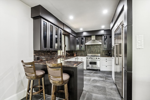 kitchen with tasteful backsplash, designer stove, a kitchen breakfast bar, kitchen peninsula, and wall chimney exhaust hood